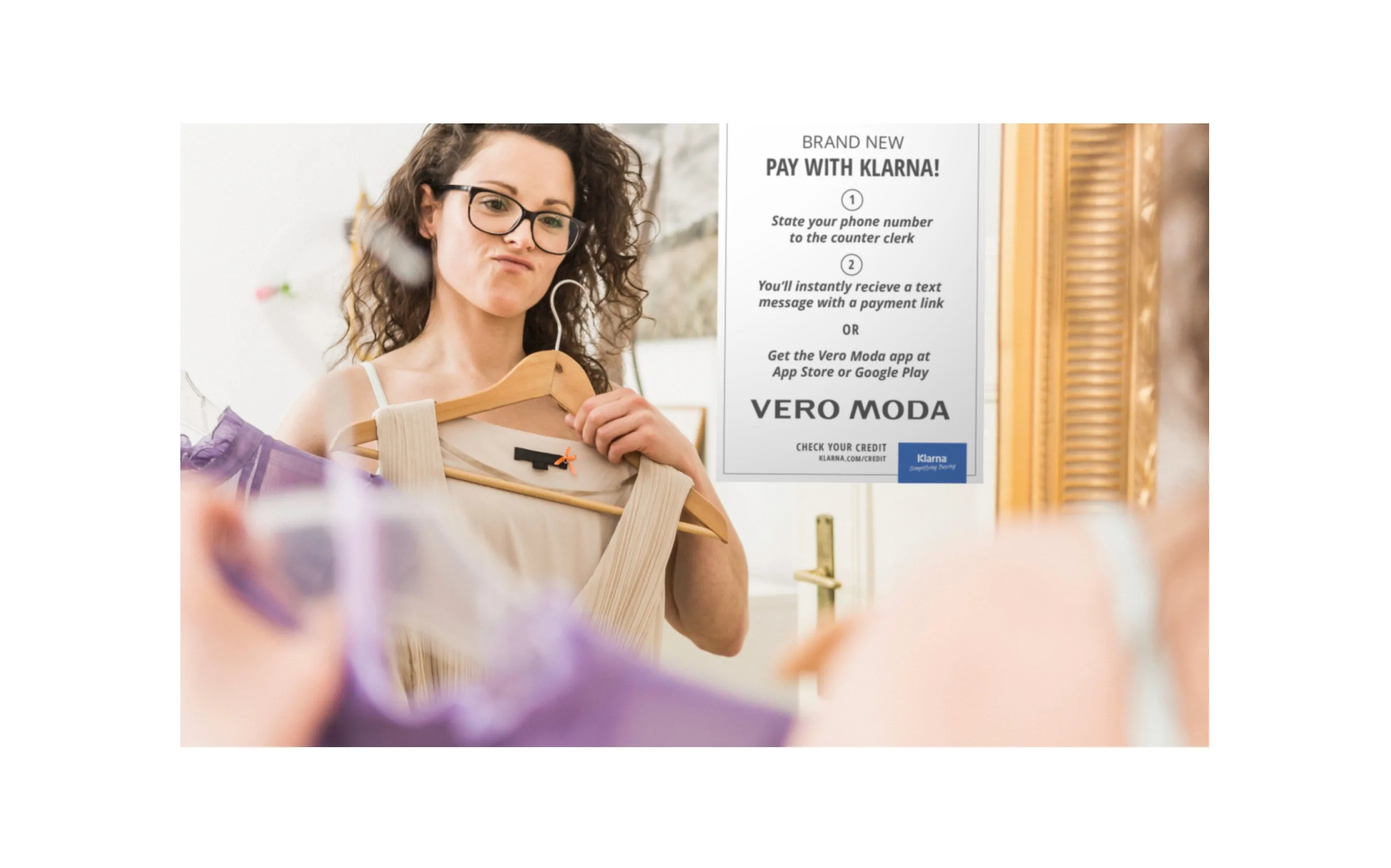 A customer tries on a dress in a Vero Moda fitting room, next to a “Pay with Klarna” sign explaining how to pay in store